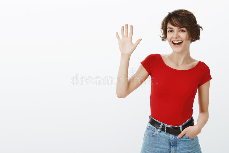 Hé ce qui est La coupe de cheveux courte de fille européenne amicale gaie sociable attirante ondulant la paume augmentée indique images stock Hé ce qui est La coupe de cheveux courte de fille européenne amicale gaie sociable attirante ondulant la paume augmentée indique images stock