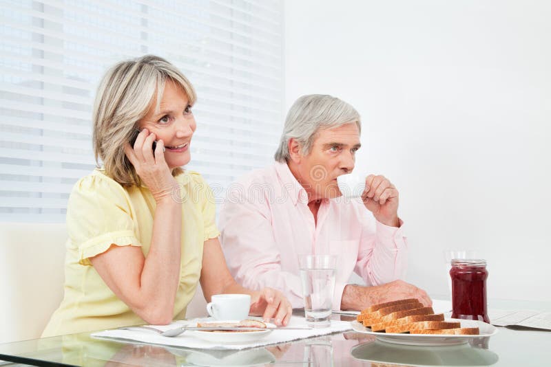Senior women using her cell phone at breakfast table. Senior women using her cell phone at breakfast table