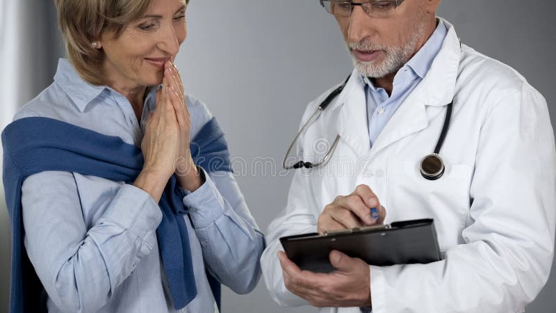 Hög dam som är lycklig att höra behandlingresultat, doktor som berättar goda nyheter, framsteg arkivfoto Hög dam som är lycklig att höra behandlingresultat, doktor som berättar goda nyheter, framsteg arkivfoto