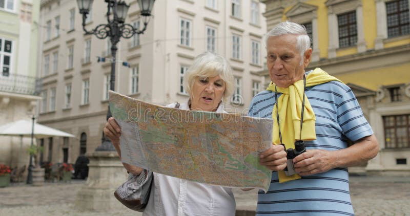 Hög man och kvinnliga turister som står med en översikt i händer som söker efter rutten royaltyfria foton Hög man och kvinnliga turister som står med en översikt i händer som söker efter rutten royaltyfria foton