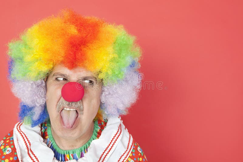 Hög manlig clown som ut klibbar tungan, medan se bort över röd bakgrund arkivfoto Hög manlig clown som ut klibbar tungan, medan se bort över röd bakgrund arkivfoto