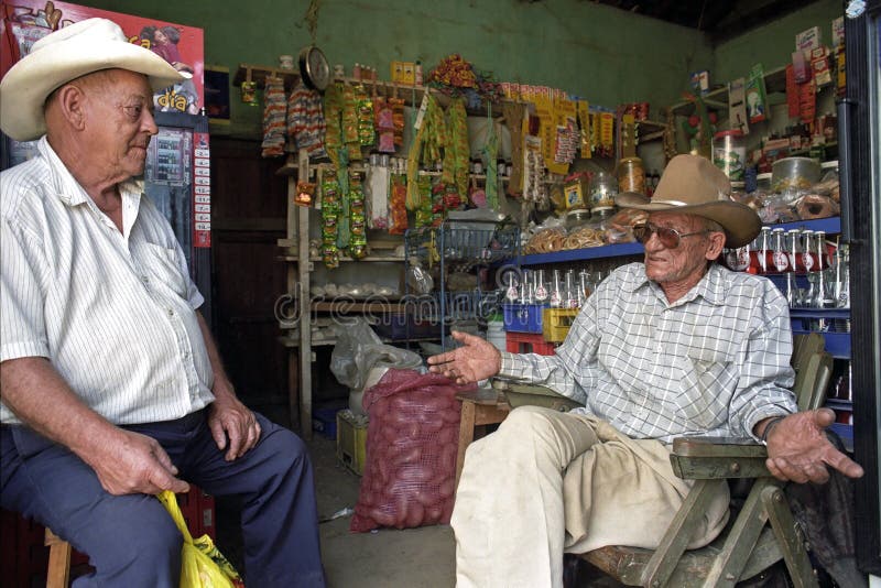 Nicaragua, department Nueva Segovia, Ocotal city: close-up of men in grocery. Elderly man on the right is the owner of the shop. The old man on the left is a friend and buyer who has purchased merchandise. They talk about the political situation in the country. Behind the elderly the goods are on display: such as potatoes, cookies, candy and soda. Nicaragua, department Nueva Segovia, Ocotal city: close-up of men in grocery. Elderly man on the right is the owner of the shop. The old man on the left is a friend and buyer who has purchased merchandise. They talk about the political situation in the country. Behind the elderly the goods are on display: such as potatoes, cookies, candy and soda.