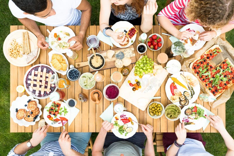 Hög vinkel av vänner som äter pizza och frukt under en celebratio royaltyfri foto Hög vinkel av vänner som äter pizza och frukt under en celebratio royaltyfri foto