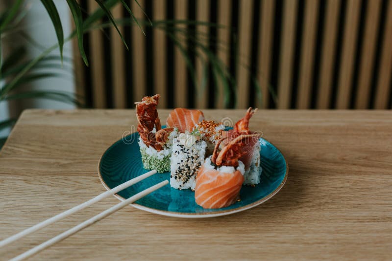 Hög vinkelbild av en vacker blå platta fylld med olika typer av sushi på ett träbord arkivbilder Hög vinkelbild av en vacker blå platta fylld med olika typer av sushi på ett träbord arkivbilder