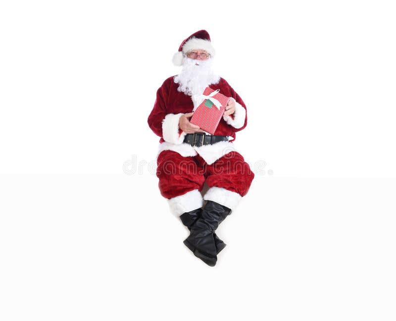 Högre man i den traditionella juldräkten som sitter på en vit vägg och håller en omsluten present