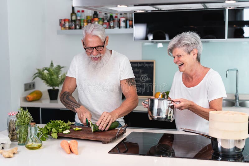 Högre par matlagning hemma när man förbereder vegetariska lunchen könade människor som skär grönsaker för hälsosam måltid i huset arkivbilder