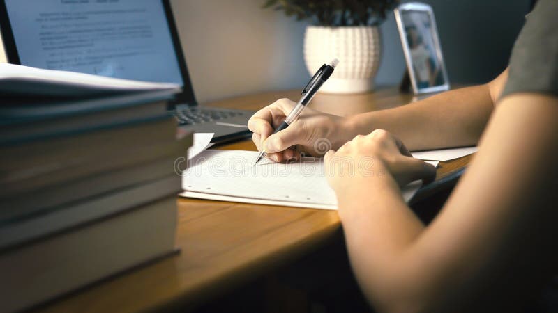 College or university student doing school homework at home. Working late at night. Young woman writing on paper with pen. Girl doing math task. Person using laptop on desk. College or university student doing school homework at home. Working late at night. Young woman writing on paper with pen. Girl doing math task. Person using laptop on desk