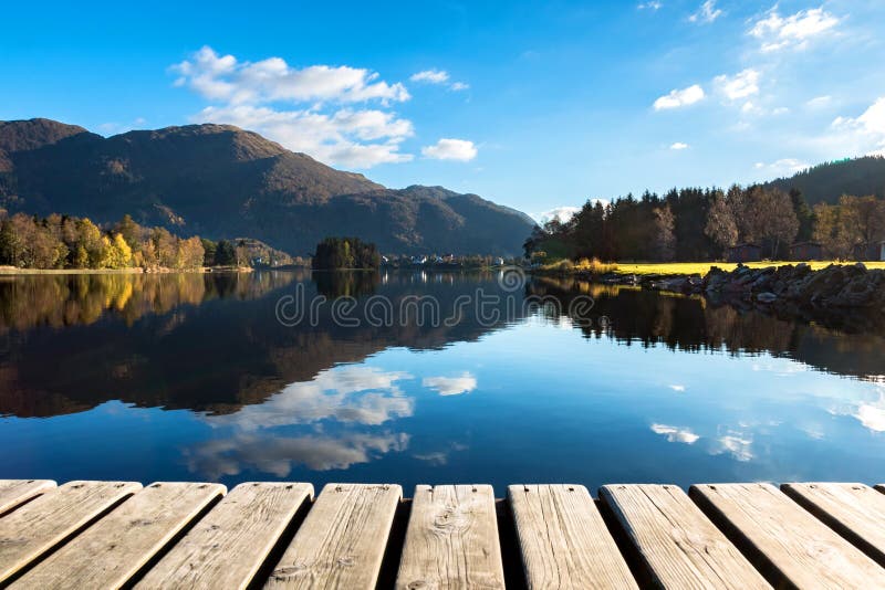 Hölzerne Beschaffenheit und schöner Autumn Landscape Background mit bunten Bäumen, Bergen, Wolken im blauen Himmel und See-Reflex lizenzfreie stockfotografie