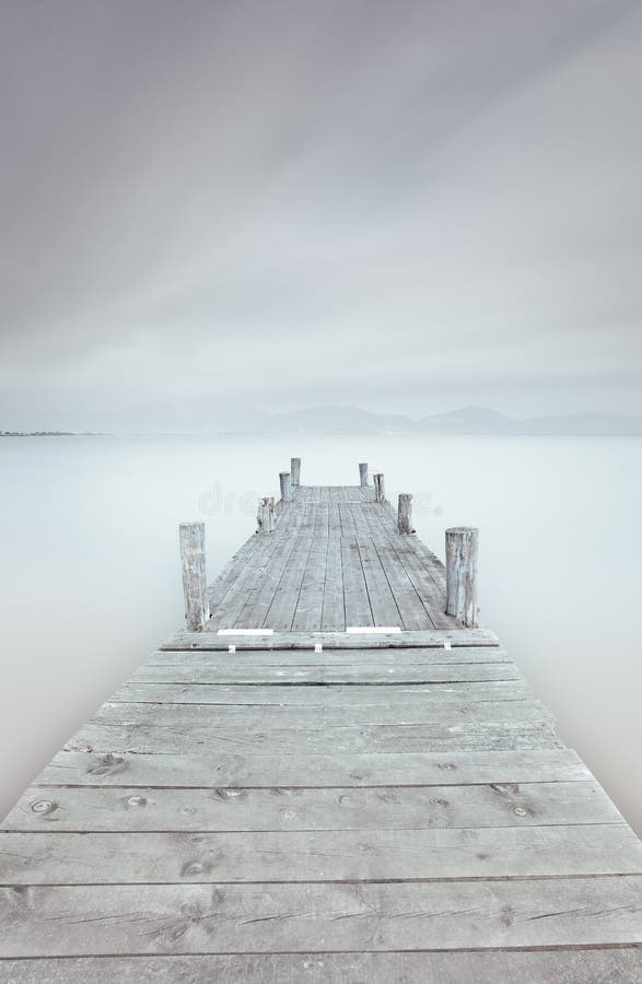 Hölzerner Pier auf See in einer bewölkten und nebeligen Stimmung.