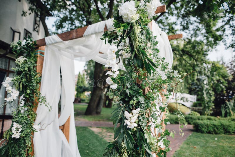 Hölzernes Zeremoniebogen decoretade durch weißen Stoff, Blumen und gree