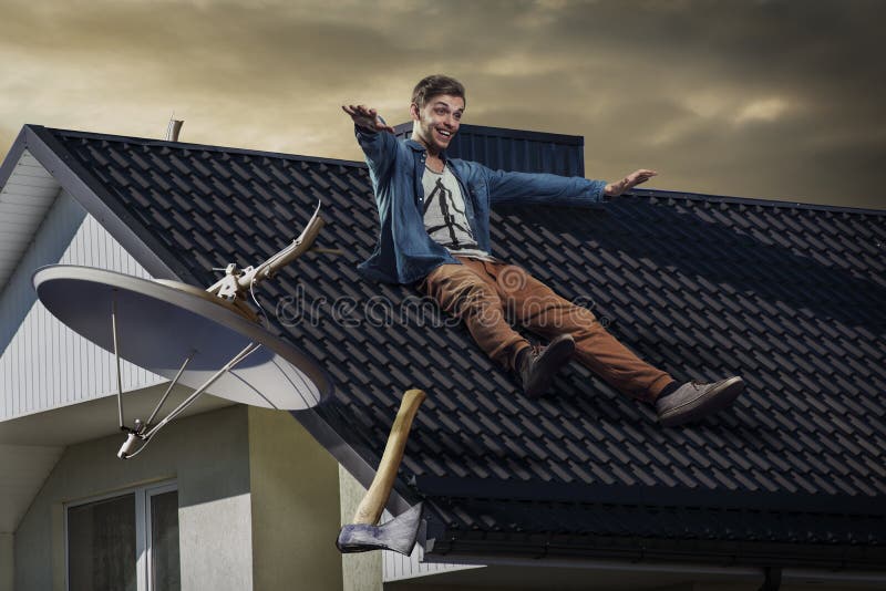 Young crazy happy man sliding down off the roof. He chopped off satellite Tv antenna with an axe. Breaking the habit- no more watching Tv at home. Young crazy happy man sliding down off the roof. He chopped off satellite Tv antenna with an axe. Breaking the habit- no more watching Tv at home.