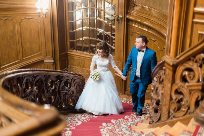 Hübsche Braut und hübscher Bräutigam, die in Richtung des Gehens herauf alte hölzerne Treppe auf dem Hintergrund des Luxusinnenra lizenzfreies stockfoto Hübsche Braut und hübscher Bräutigam, die in Richtung des Gehens herauf alte hölzerne Treppe auf dem Hintergrund des Luxusinnenra lizenzfreies stockfoto