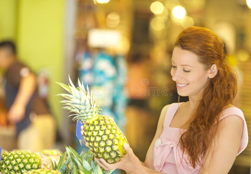 Hübsche Frau, die Ananas beim Einkauf im Gemischtwarenladen wählt stockfotos Hübsche Frau, die Ananas beim Einkauf im Gemischtwarenladen wählt stockfotos