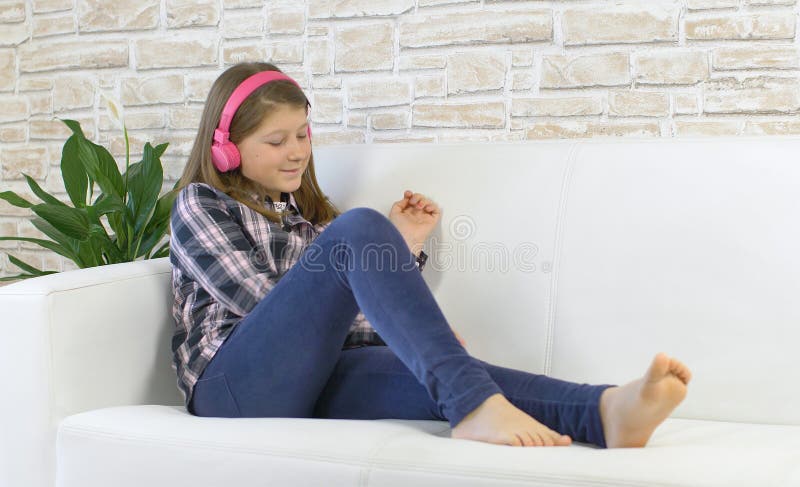 Hübsche junge Mädchen tanzen und hören Musik mit Kopfhörern auf weißem Sofa zu Hause stockfoto