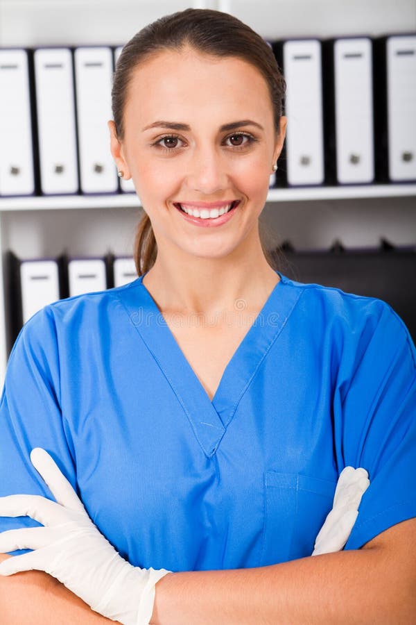 A pretty young nurse in scrubs standing in hospital office with patients records in files behind her. A pretty young nurse in scrubs standing in hospital office with patients records in files behind her