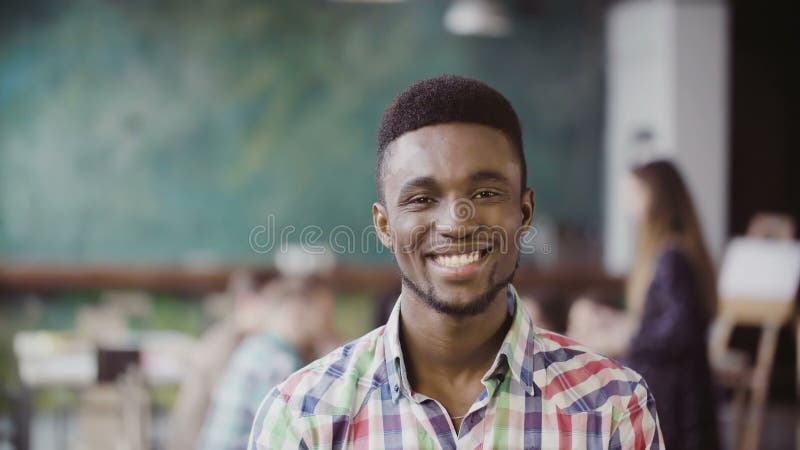 Hübscher afrikanischer Mann im beschäftigten modernen Büro Porträt des jungen erfolgreichen Mannes, der Kamera und das Lächeln be lizenzfreies stockbild Hübscher afrikanischer Mann im beschäftigten modernen Büro Porträt des jungen erfolgreichen Mannes, der Kamera und das Lächeln be lizenzfreies stockbild