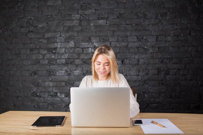 Hübscher Frauenwerbetexter, der im Internet auf dem tragbaren Netzbuch, sitzend im Büro arbeitet stockfotos