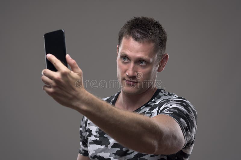 Hübscher junger Mann im Tarnungsmustert-shirt, das Fotos mit Handy macht lizenzfreies stockfoto