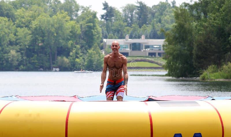 Hübscher netter Mann, der an einer Wassertrampoline schwimmt in einen See in Michigan während des Sommers springt stockbild Hübscher netter Mann, der an einer Wassertrampoline schwimmt in einen See in Michigan während des Sommers springt stockbild