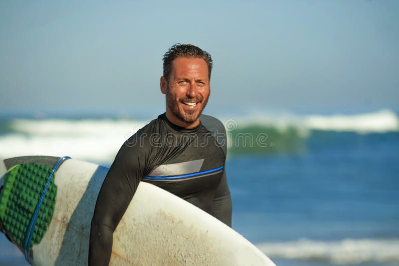 Hübscher und attraktiver Surfermann Brandungsbrettlächeln des Neoprenbadeanzugs im tragenden glücklich und nett, nachdem das Geni lizenzfreie stockbilder Hübscher und attraktiver Surfermann Brandungsbrettlächeln des Neoprenbadeanzugs im tragenden glücklich und nett, nachdem das Geni lizenzfreie stockbilder