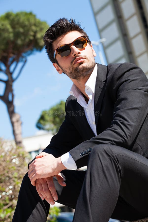 Hübscher und reizend junger Mann mit der Sonnenbrille, die draußen sitzt