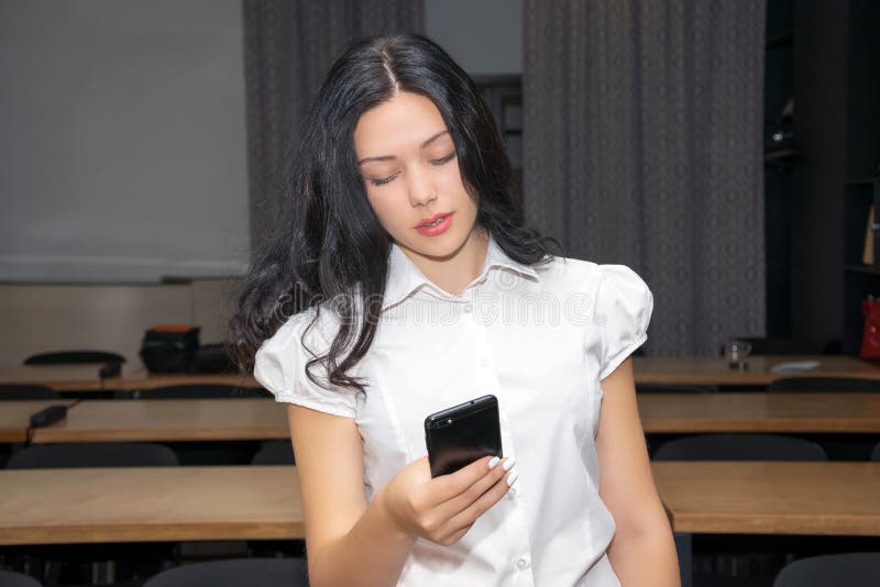 Hübsches Mädchen im Klassenzimmer mit Smartphone in den Händen, Schirm betrachtend Schließen Sie herauf Foto stockfotografie Hübsches Mädchen im Klassenzimmer mit Smartphone in den Händen, Schirm betrachtend Schließen Sie herauf Foto stockfotografie