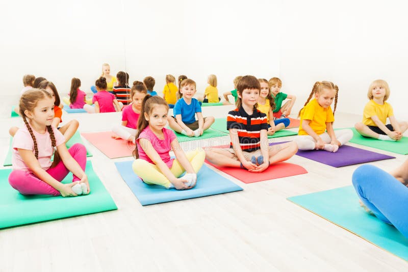 Portrait of 5-6 years old boys and girls doing butterfly exercise sitting on yoga mats in gym. Portrait of 5-6 years old boys and girls doing butterfly exercise sitting on yoga mats in gym