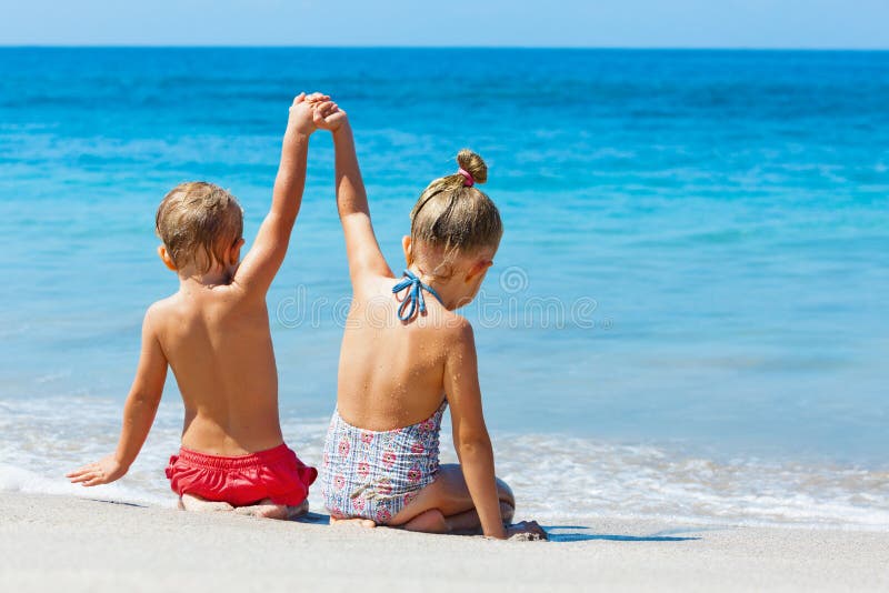 Happy kids have fun in sea surf on white sand beach. Couple of children sit in water pool with hands up. Travel lifestyle, swimming activities in family summer camp. Vacations on tropical island. Happy kids have fun in sea surf on white sand beach. Couple of children sit in water pool with hands up. Travel lifestyle, swimming activities in family summer camp. Vacations on tropical island.