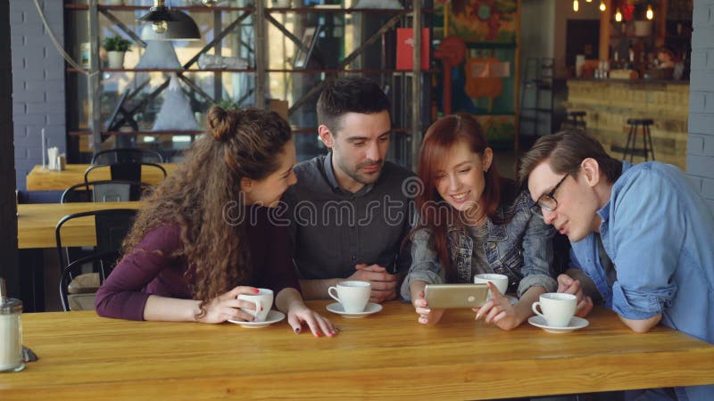 I belli amici stanno guardando il video interessante e stanno discutendolo mentre bevevano il tè alla tavola in caffè accogliente