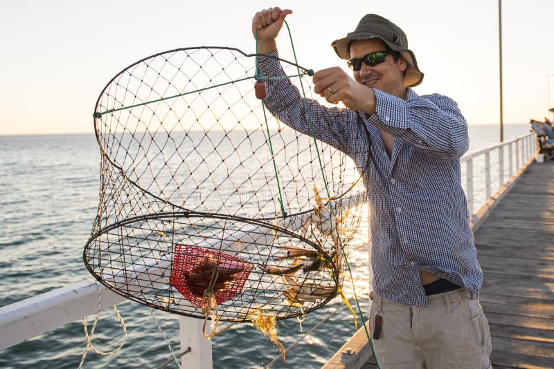 I bloccaggi attraenti fieri della rete del canestro del pesce e dei granchi di rappresentazione del pescatore che sorridono in ma immagini stock libere da diritti I bloccaggi attraenti fieri della rete del canestro del pesce e dei granchi di rappresentazione del pescatore che sorridono in ma immagini stock libere da diritti