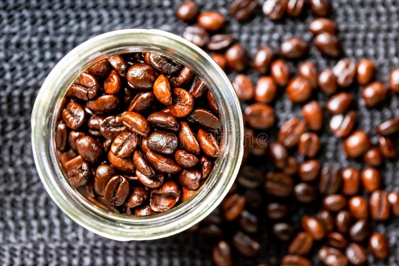 I chicchi di caffè arrostiti, medium hanno arrostito nella bottiglia di vetro e sulla rete nera fotografia stock I chicchi di caffè arrostiti, medium hanno arrostito nella bottiglia di vetro e sulla rete nera fotografia stock