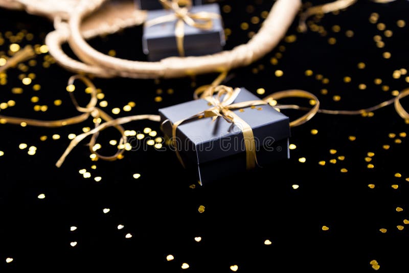 I contenitori di regalo neri con il nastro dell'oro schioccano fuori dalla borsa dorata sul fondo di lustro Fine in su fotografia stock I contenitori di regalo neri con il nastro dell'oro schioccano fuori dalla borsa dorata sul fondo di lustro Fine in su fotografia stock