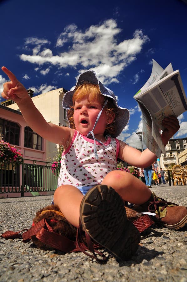 Bambina con una mappa in mano e si punta verso qualcosa, mentre siede su un zaino in Chamonix piazza.