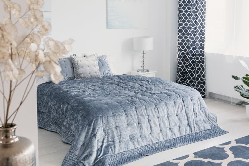 I fiori in camera da letto elegante bianca interna con gli strati blu sul letto accanto alla lampada e copre Foto reale