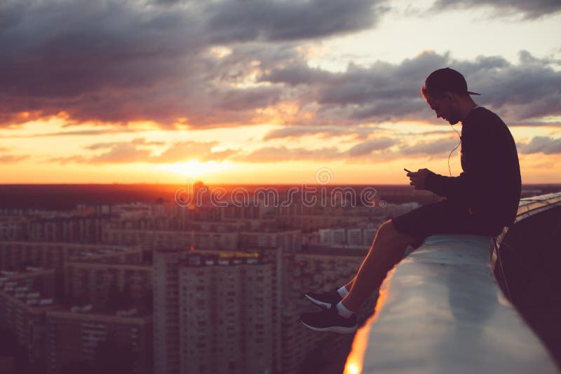I giovani sfidano l'uomo che si siede sopra la città con lo smartphone al tramonto