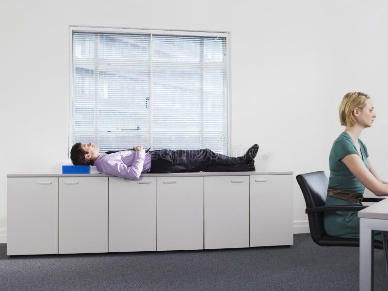 I Governi di Sleeps On Office dell'uomo d'affari si avvicinano al funzionamento della donna fotografie stock libere da diritti I Governi di Sleeps On Office dell'uomo d'affari si avvicinano al funzionamento della donna fotografie stock libere da diritti