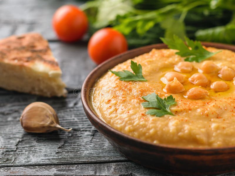 I hummus appena fatti in un'argilla lanciano su una tavola con un pezzo di pane immagini stock