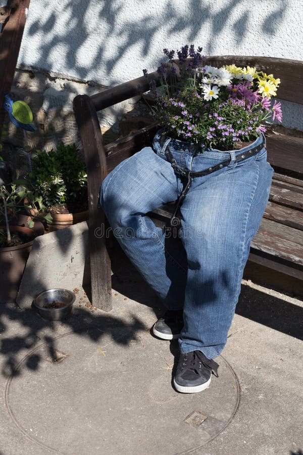 i jeans di taglio decorati con i fiori che si siedono su un giardino bench la a fotografia stock i jeans di taglio decorati con i fiori che si siedono su un giardino bench la a fotografia stock