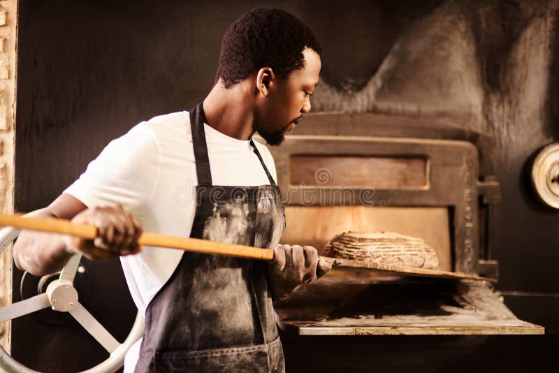 I make them fresh every day. a male baker removing freshly baked bread from the oven.