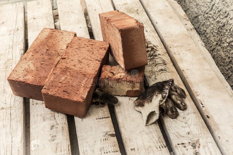 I mattoni rossi ed i guanti sporchi usati su un pallet delle plance, fondo astratto della costruzione immagini stock libere da diritti I mattoni rossi ed i guanti sporchi usati su un pallet delle plance, fondo astratto della costruzione immagini stock libere da diritti
