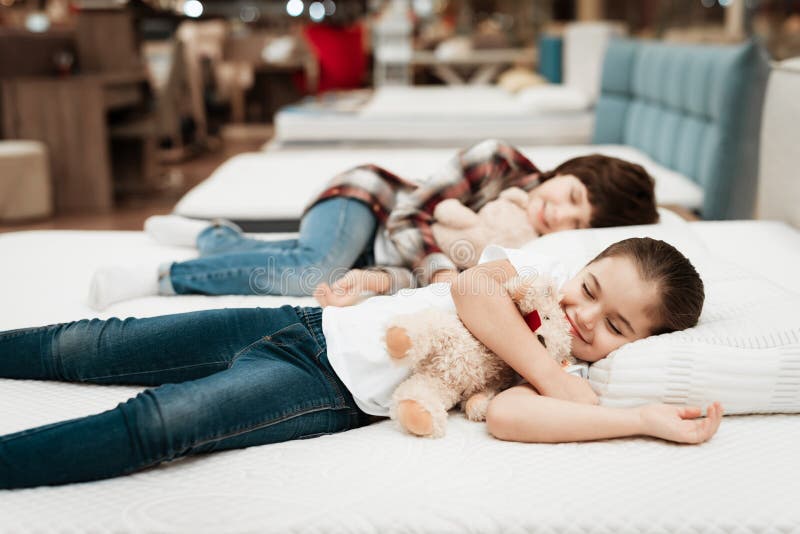 I piccoli abbracci felici della ragazza sopportano trovarsi sul letto Nei sonni del ragazzino del fondo immagini stock