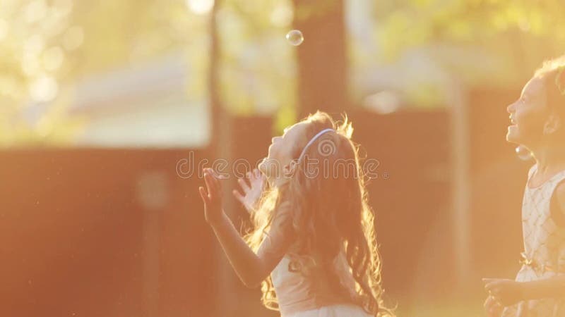 I piccoli bambini europei sono saltanti e giocanti con le bolle di sapone ad una luce del tramonto Chiarore della lente, fucilazi