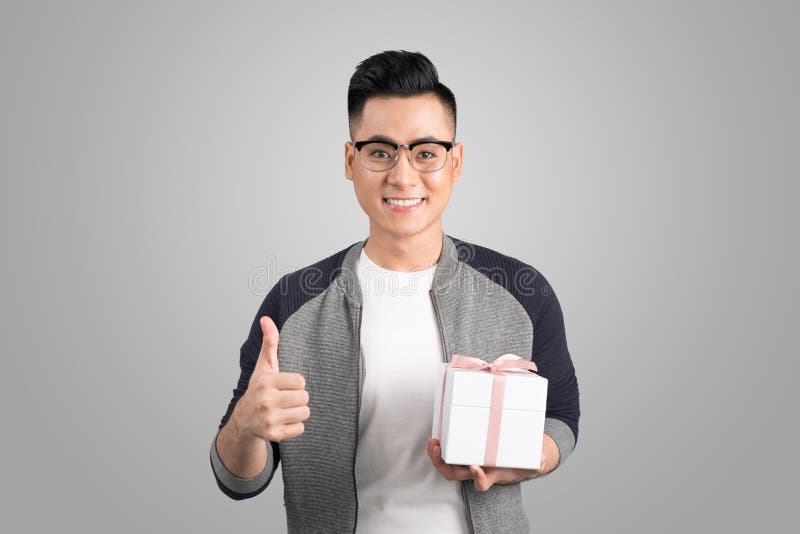 I pollici asiatici dell'uomo aumentano ed il contenitore di regalo della tenuta Colpo dello studio, parte posteriore di gray fotografia stock libera da diritti I pollici asiatici dell'uomo aumentano ed il contenitore di regalo della tenuta Colpo dello studio, parte posteriore di gray fotografia stock libera da diritti