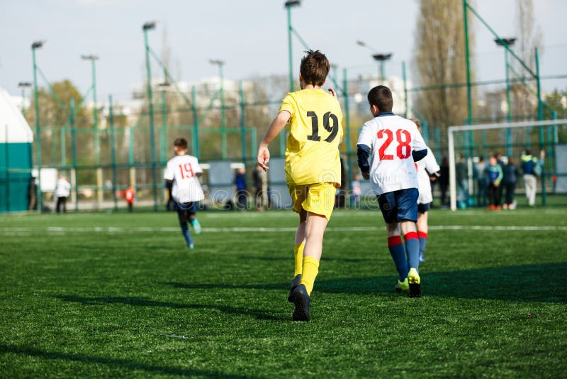 I ragazzi delle squadre di football americano in abiti sportivi bianchi gialli giocano a calcio sul campo verde abilit? di goccio fotografia stock