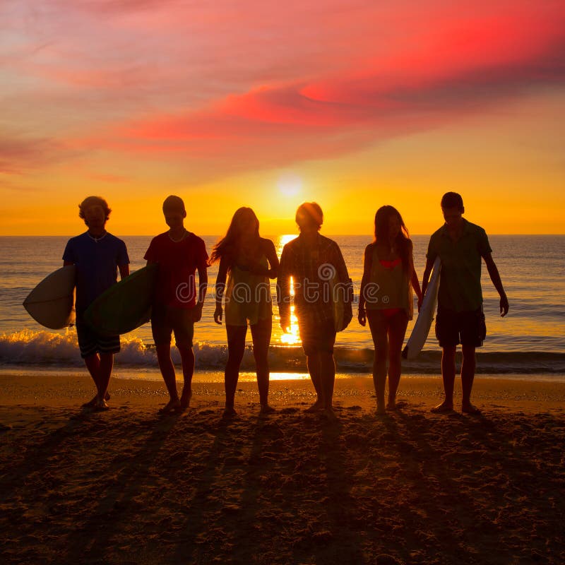 I ragazzi e le ragazze dei surfisti raggruppano la camminata sulla spiaggia