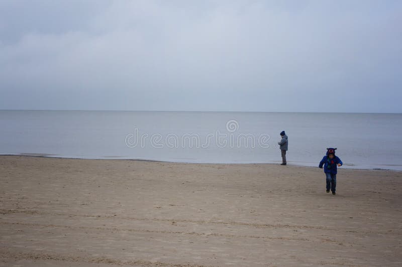 I ragazzini sta sulla spiaggia il mare il giorno ventoso freddo fotografie stock libere da diritti I ragazzini sta sulla spiaggia il mare il giorno ventoso freddo fotografie stock libere da diritti