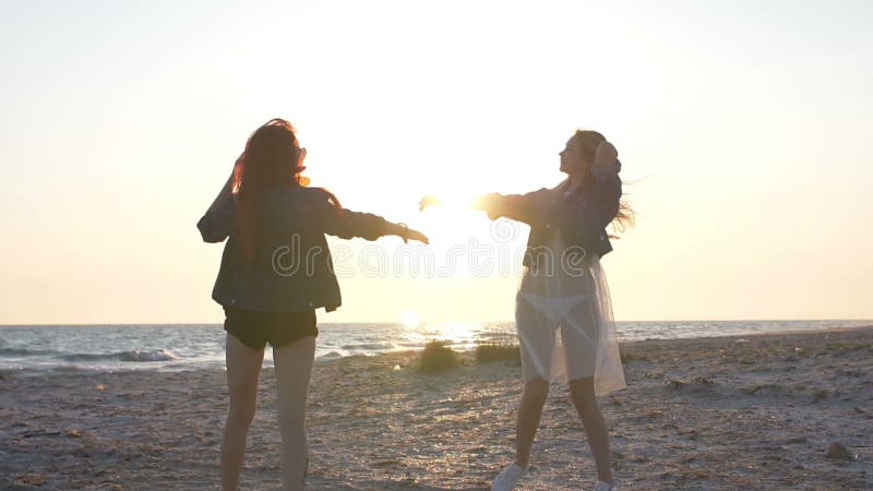 I raggi del tramonto sopra il mare illuminano il ballo sulla spiaggia di due giovani donne sexy vestite nello stile di boho