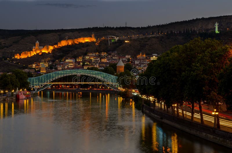 I stadens centrum Tbilisi fredbro som göras från exponeringsglas, floden Mtkvari och berömd forntida narikalafästning på kullen s arkivfoton I stadens centrum Tbilisi fredbro som göras från exponeringsglas, floden Mtkvari och berömd forntida narikalafästning på kullen s arkivfoton