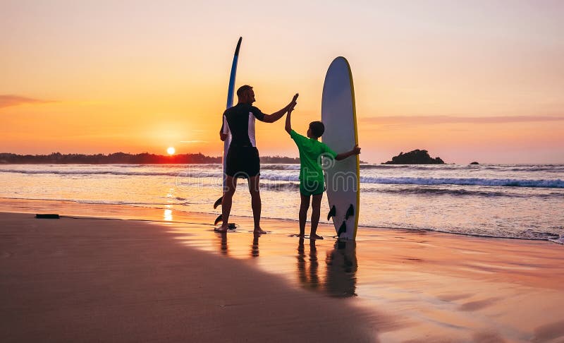I surfisti del figlio e del padre restano sulla spiaggia del tramonto