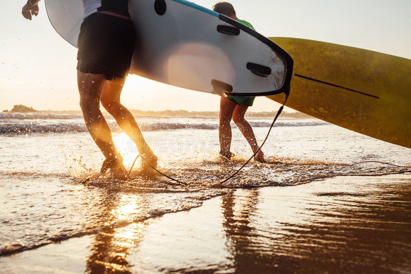 I surfisti del padre e del figlio funzionano nelle onde di oceano con i bordi praticanti il surfing